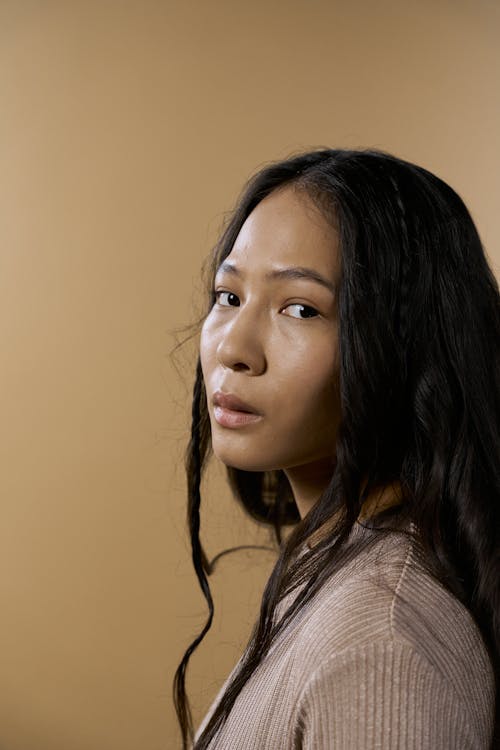 Kostnadsfri bild av asiatisk kvinna, beige bakgrund, brun topp