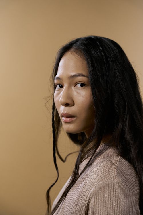 Free Studio portrait of a young East Asian woman with long hair against a brown background. Stock Photo
