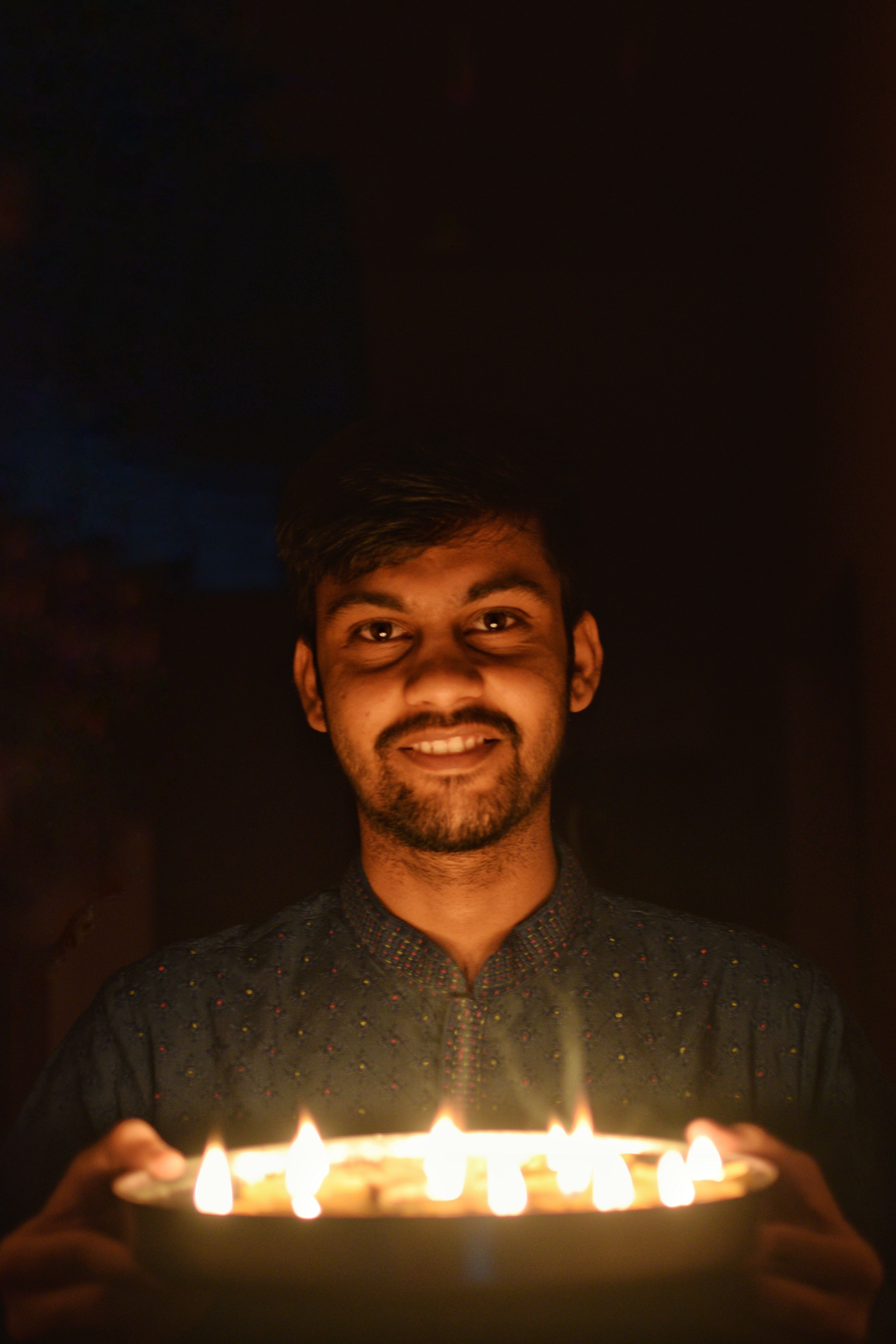 Young man with beard holds a tray of candles, creating a warm glow in a dark setting.