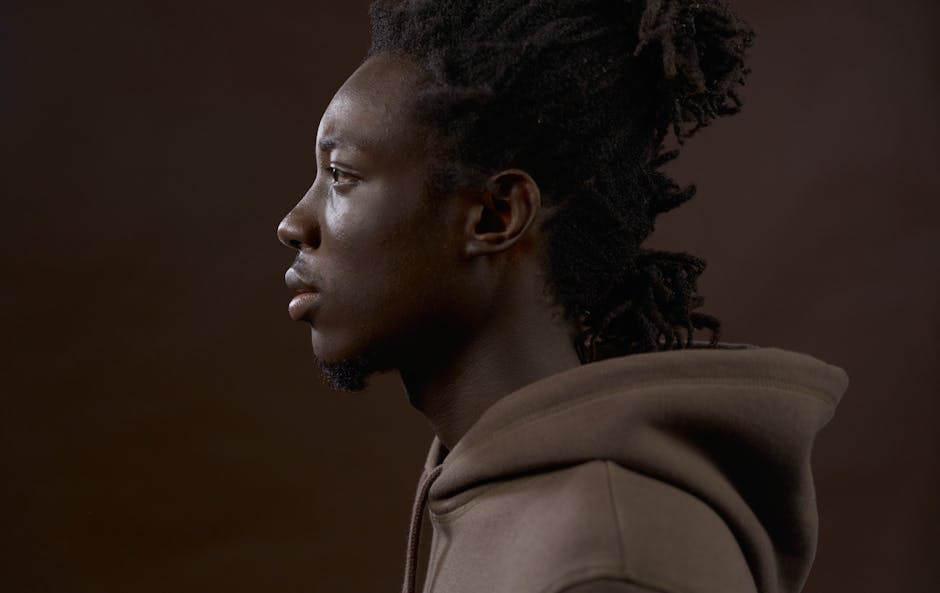 Profile portrait of a stylish man in a casual brown hoodie, set against a brown studio background.