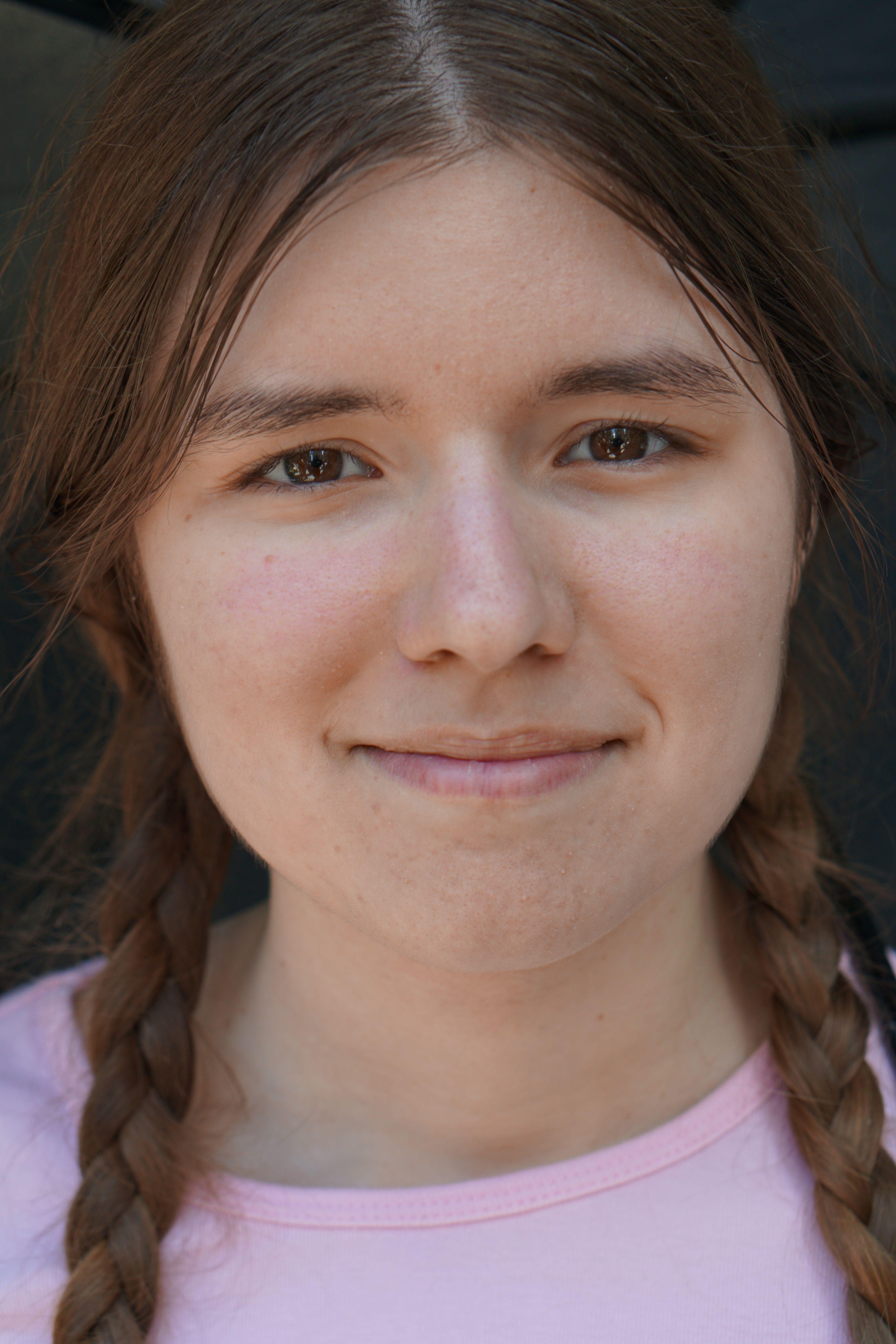 Close-up portrait of a smiling young woman with braided hair outdoors under bright daylight.