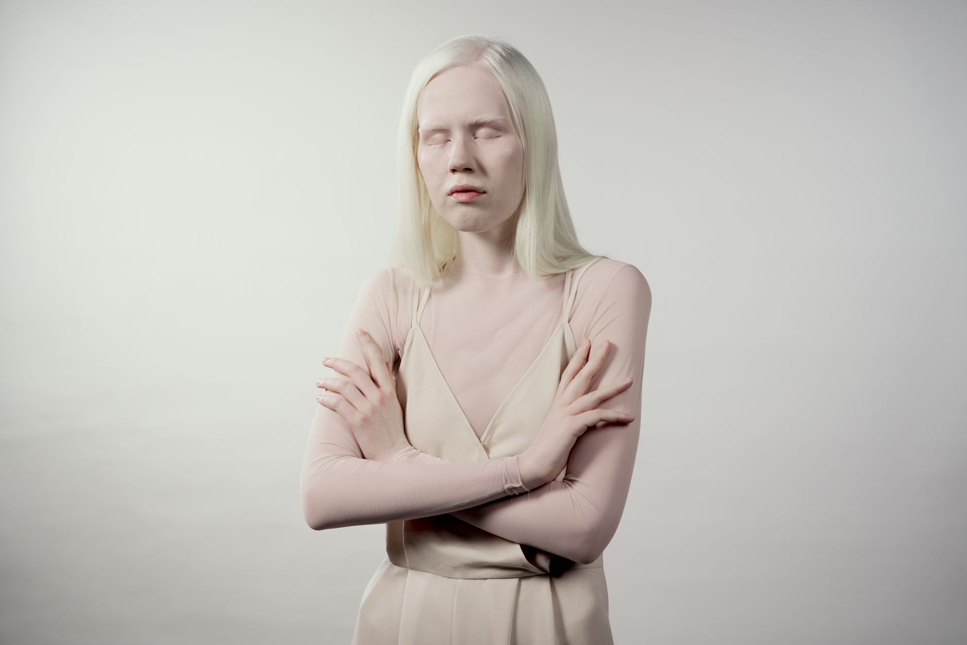 人像拍攝完整指南:對焦、測光、膚色與膚質修復技巧 Striking portrait of a young albino woman with arms crossed against a light background, exuding serene confidence.