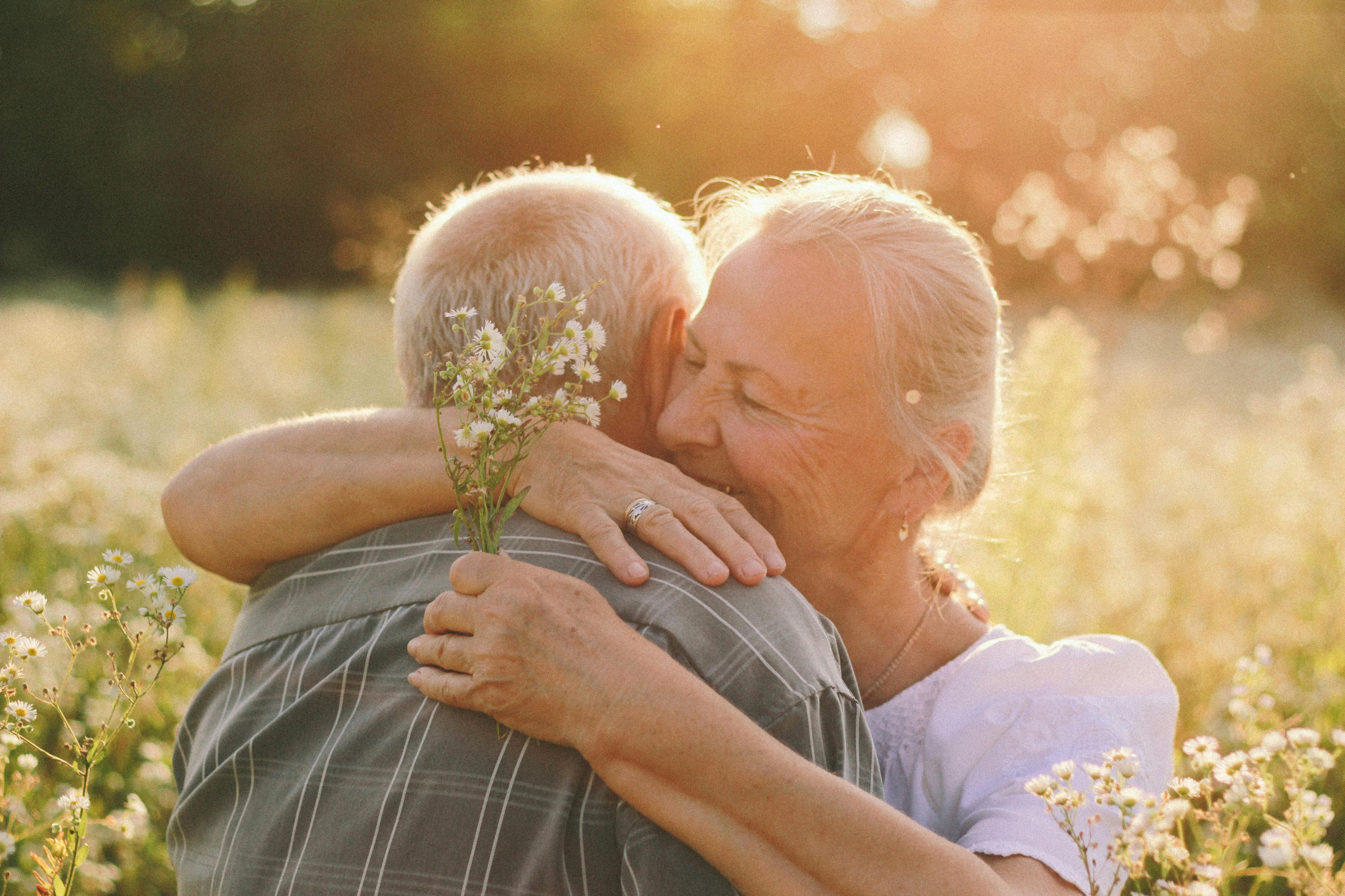 A senior couple embraces joyfully in a sunny meadow, capturing a moment of happiness and love.