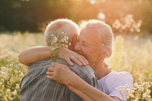 A senior couple embraces joyfully in a sunny meadow, capturing a moment of happiness and love.