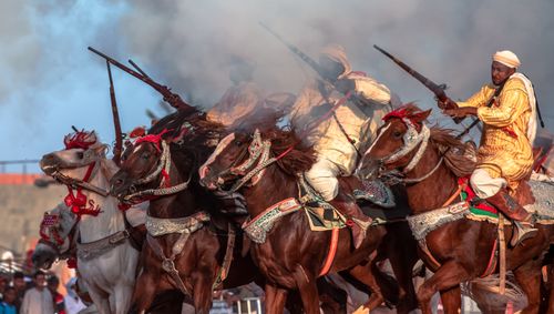 Free An exciting display of Algerian fantasia with men in traditional attire riding horses and firing rifles. Stock Photo