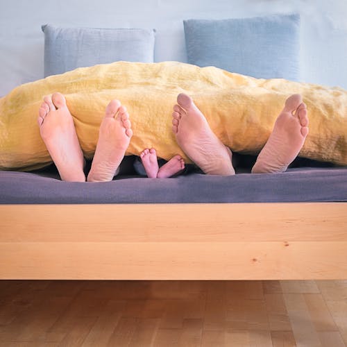 Free Family of Three Lying on Bed Showing Feet While Covered With Yellow Blanket Stock Photo