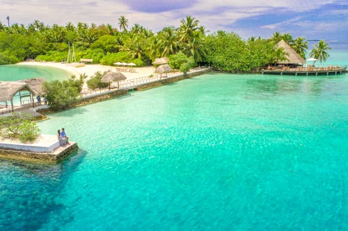 Aerial view of a couple relaxing at a tropical island resort in the Maldives, surrounded by crystal clear waters.