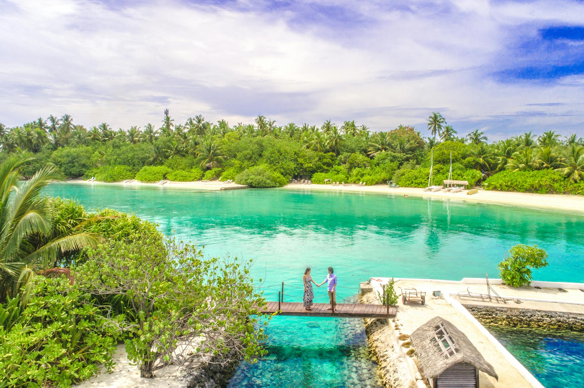 A couple holds hands on a dock overlooking the turquoise waters of the Maldives.