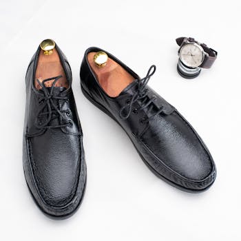 Stylish black leather shoes paired with a classic wristwatch on a white surface.