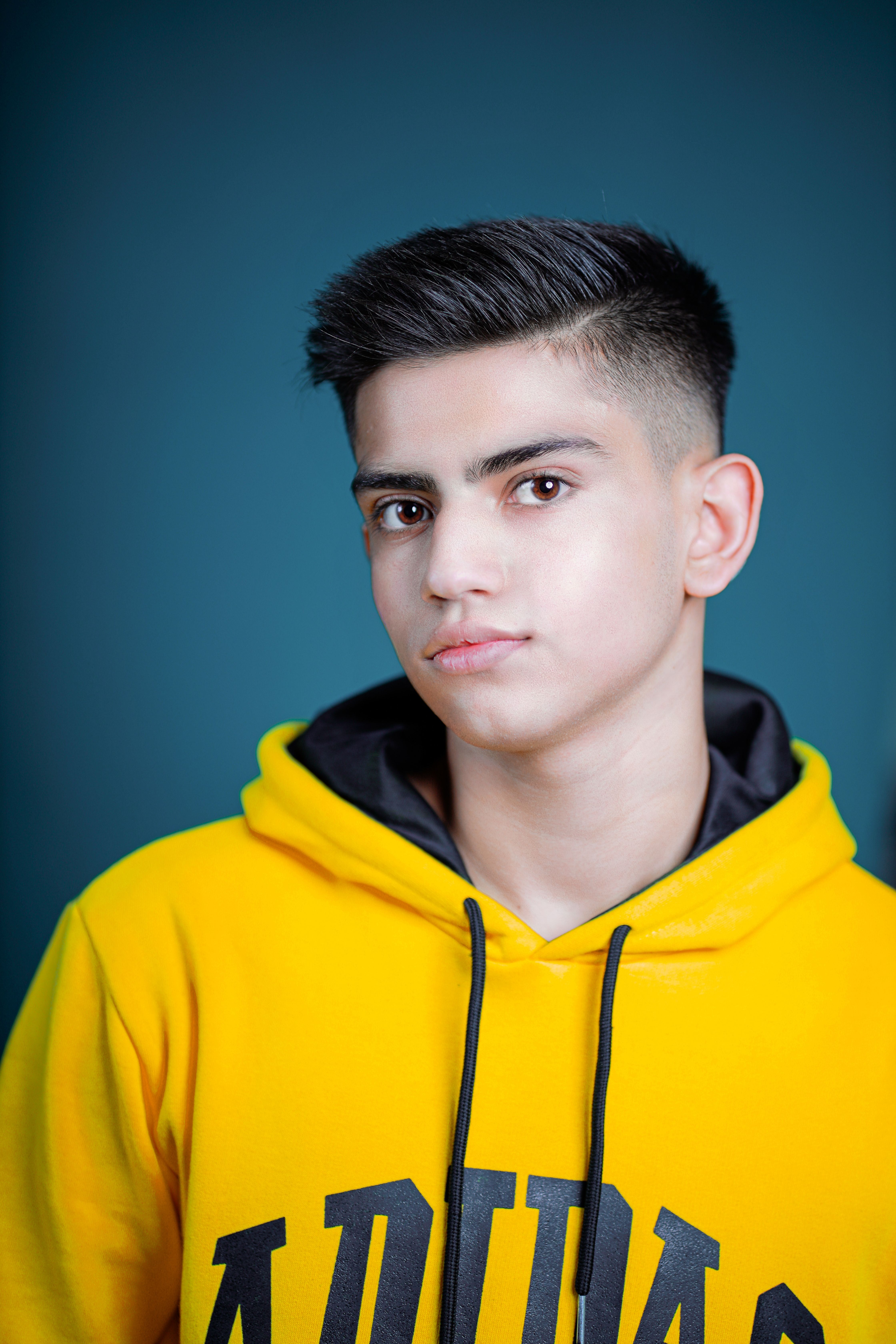 Confident teenager in a yellow hoodie posing for a portrait indoors with a bold expression.