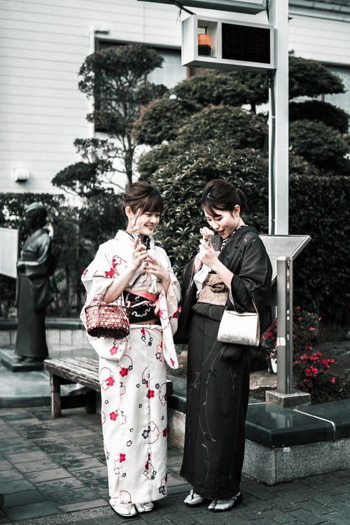 Free Two Japanese women wearing kimonos sharing a moment outdoors. Perfect blend of tradition and style. Stock Photo