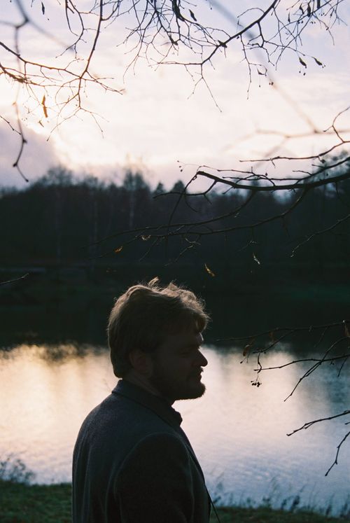 Free A man stands in silhouette by a lake during sunset, with bare trees in the foreground. Stock Photo