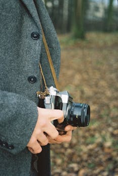 Close-up of hands holding a vintage camera outdoors during fall.
