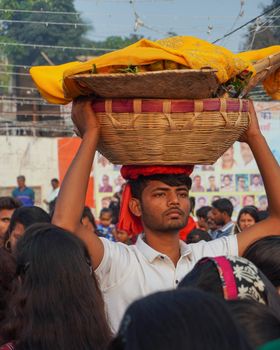 Man carries decorative basket in vibrant Indian street scene, symbolizing culture.