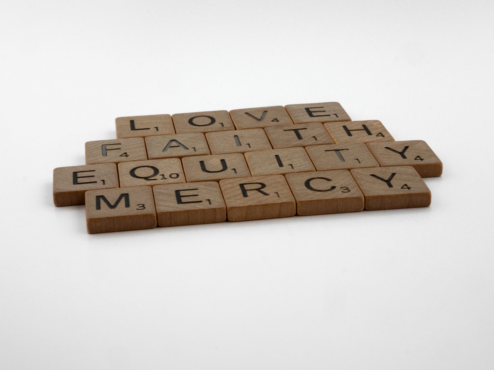 Wooden letter tiles spelling love, faith, equity, and mercy, arranged on a neutral background.