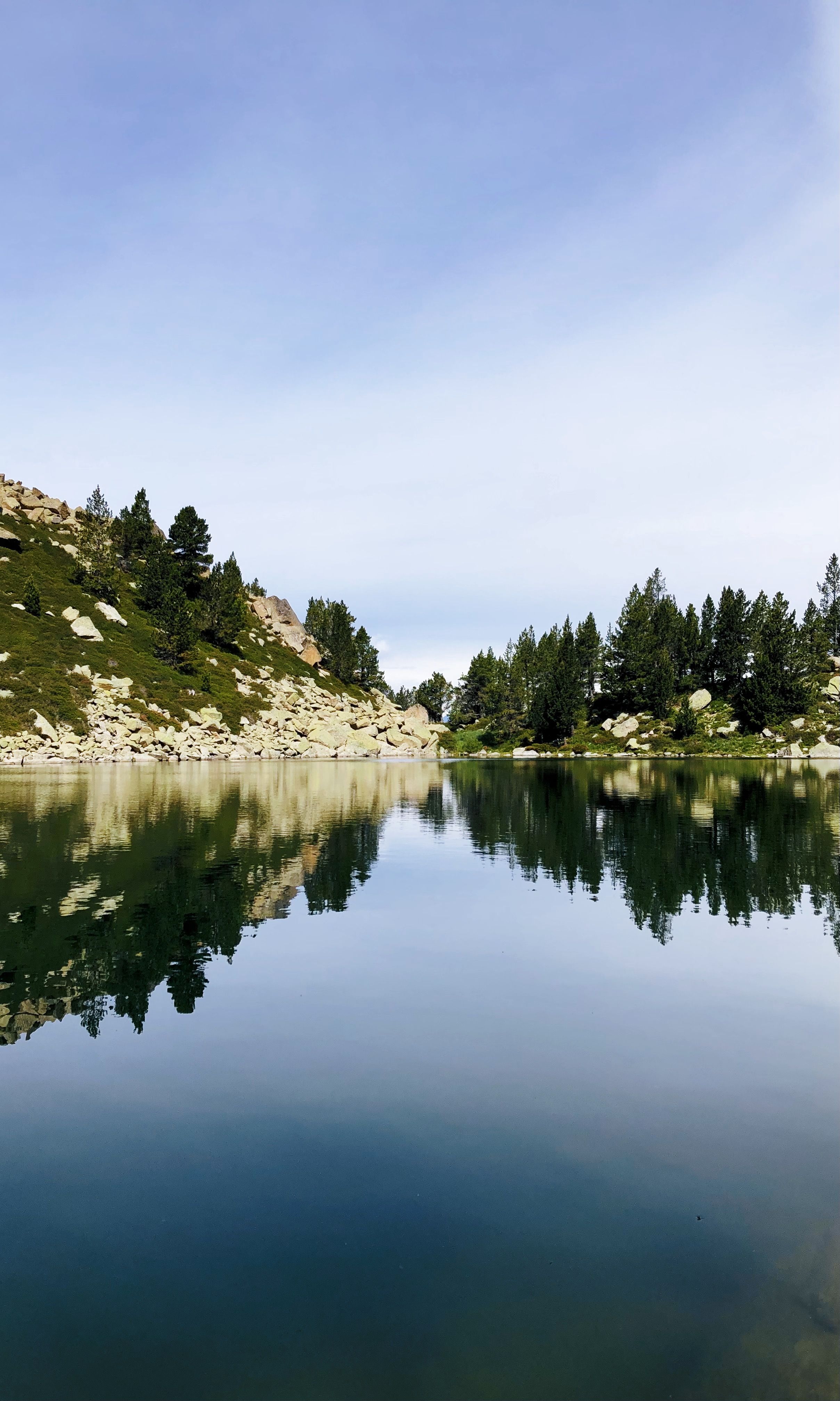 Tranquil lake with mountain backdrop and tree reflections in Encamp, Andorra. Perfect for nature lovers.