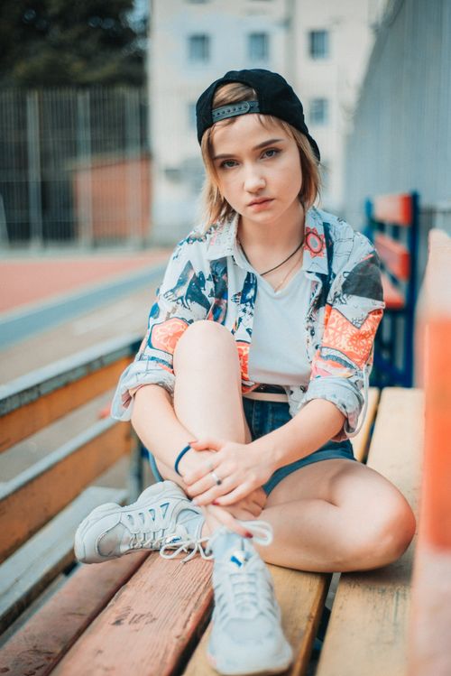Free Casual teenage girl sitting on a park bench outdoors with a relaxed expression. Stock Photo