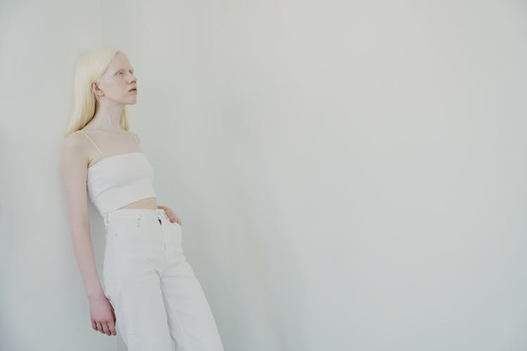 Woman In White Tank Top And White Pants Leaning On White Wall