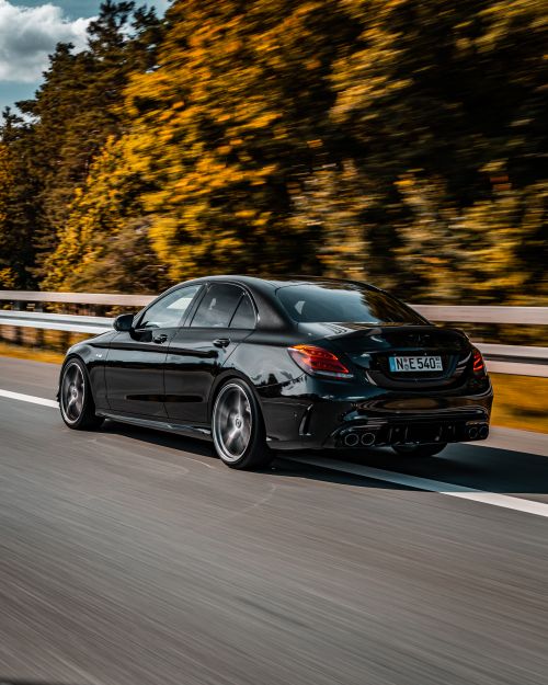 Free A sleek black luxury car drives down a picturesque highway surrounded by lush greenery. Stock Photo
