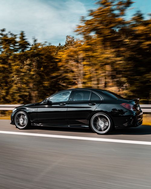Free Dynamic shot of a sleek black car speeding on a highway through a scenic forest in Nuremberg, Germany. Stock Photo