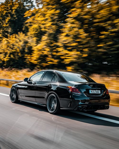 Free A sleek black car in motion on a German highway surrounded by blurred trees, showcasing speed and luxury. Stock Photo