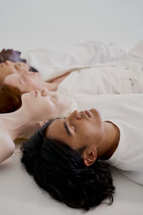 Free Diverse group of individuals lying down with eyes closed on a white surface in a studio setting. Stock Photo