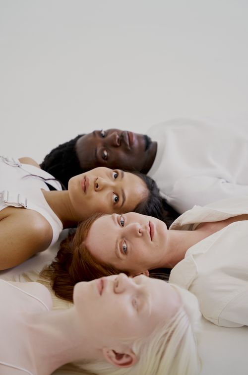 Free A diverse group of four adults lying down together indoors against a white background. Stock Photo