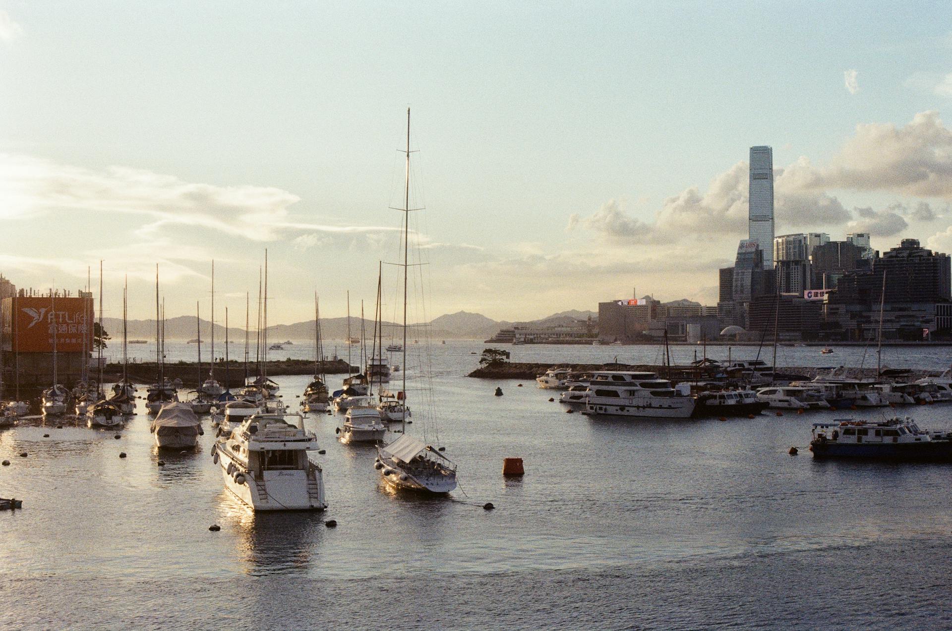 A beautiful view of boats docked in Hong Kong harbor at sunset, with city skyline and Kowloon in the background.