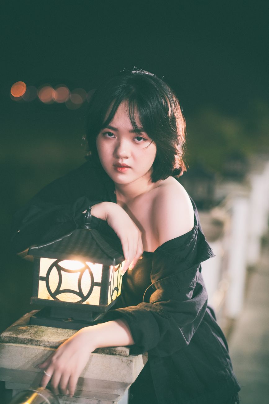 Portrait of woman in black posing by lamp with soft light at night.