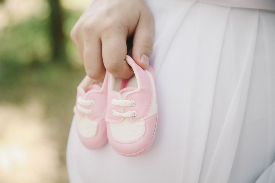 A close-up of a hand holding pink baby shoes, symbolizing new life and parenthood.