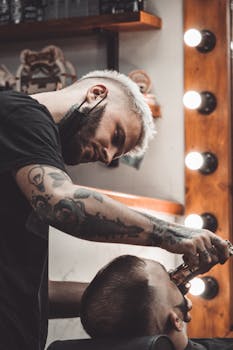 A tattooed barber trims a client's hair in a stylish salon, showcasing modern grooming techniques.