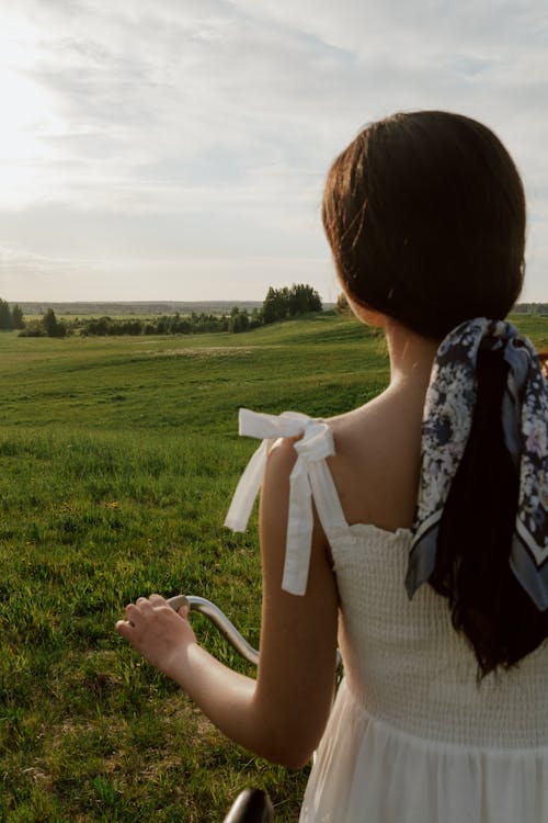 Woman in White Dress in Grass Field with Bicycle
