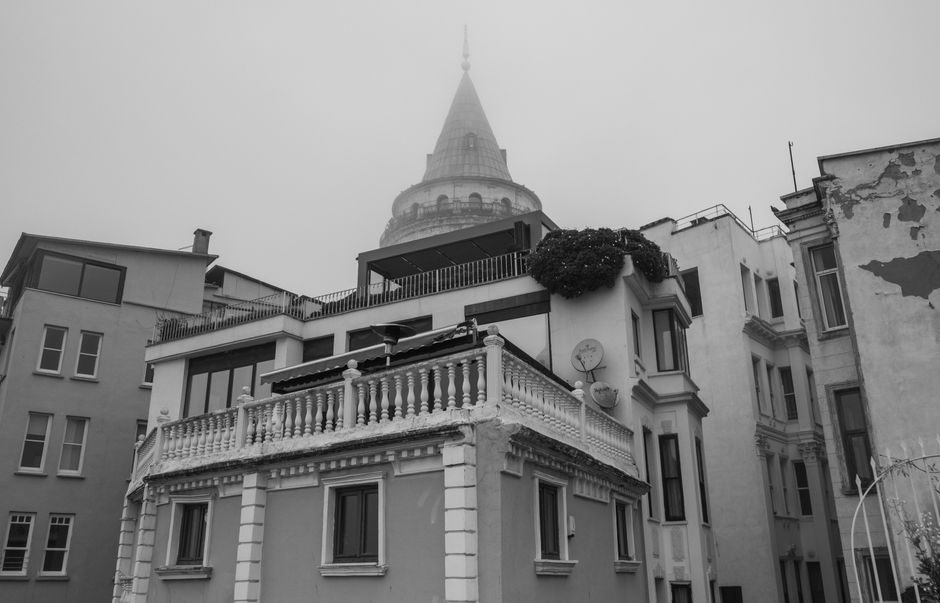 Grayscale view of Galata Tower surrounded by historic Istanbul buildings in fog.
