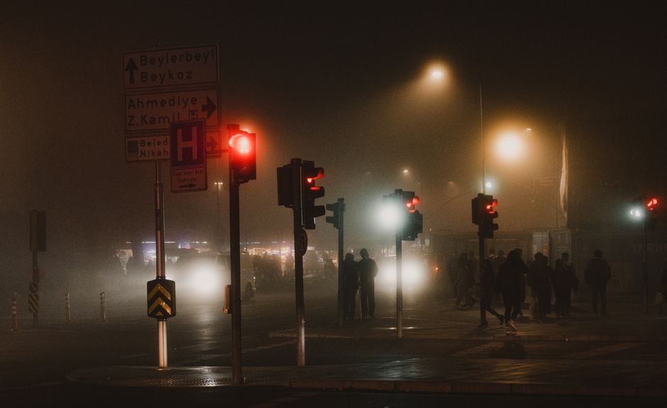 Foggy Istanbul street with people and traffic lights at night creating a mysterious atmosphere.