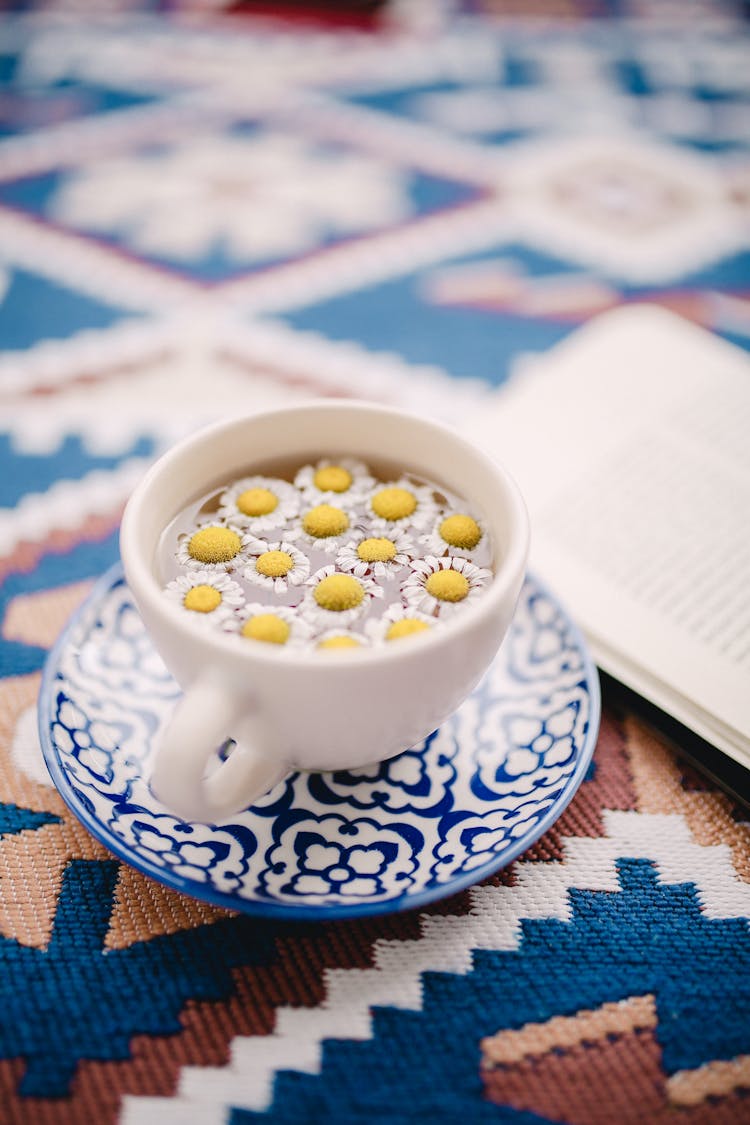 Cup Of Aromatic Camomile Tea On Ornamental Tablecloth