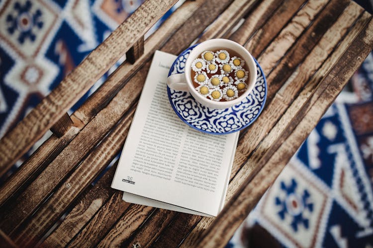 Cup Of Camomile Infusion And Magazine Laying On Wooden Bench