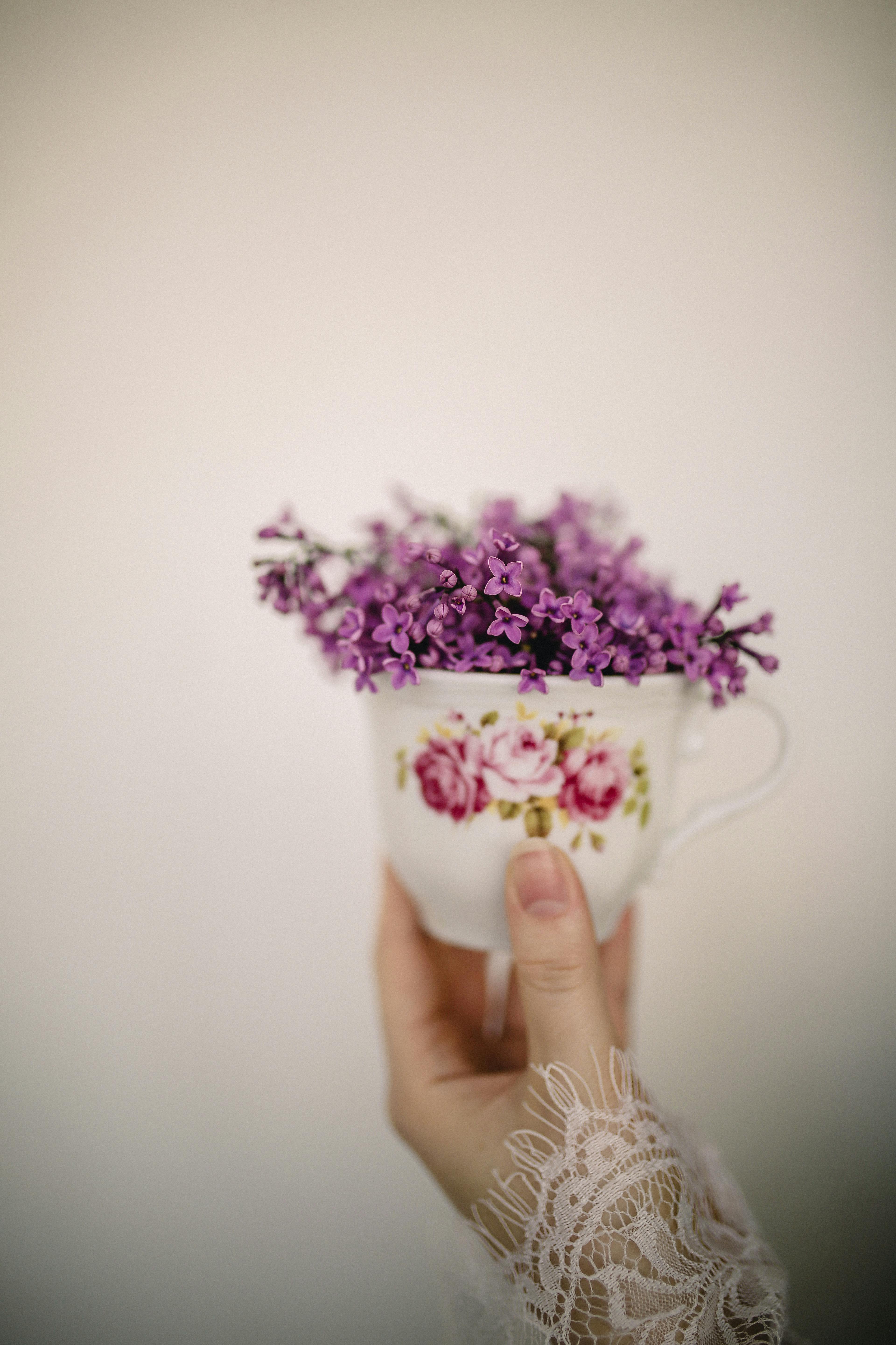 unrecognizable female hand holding ornamental vintage cup with lilac flowers