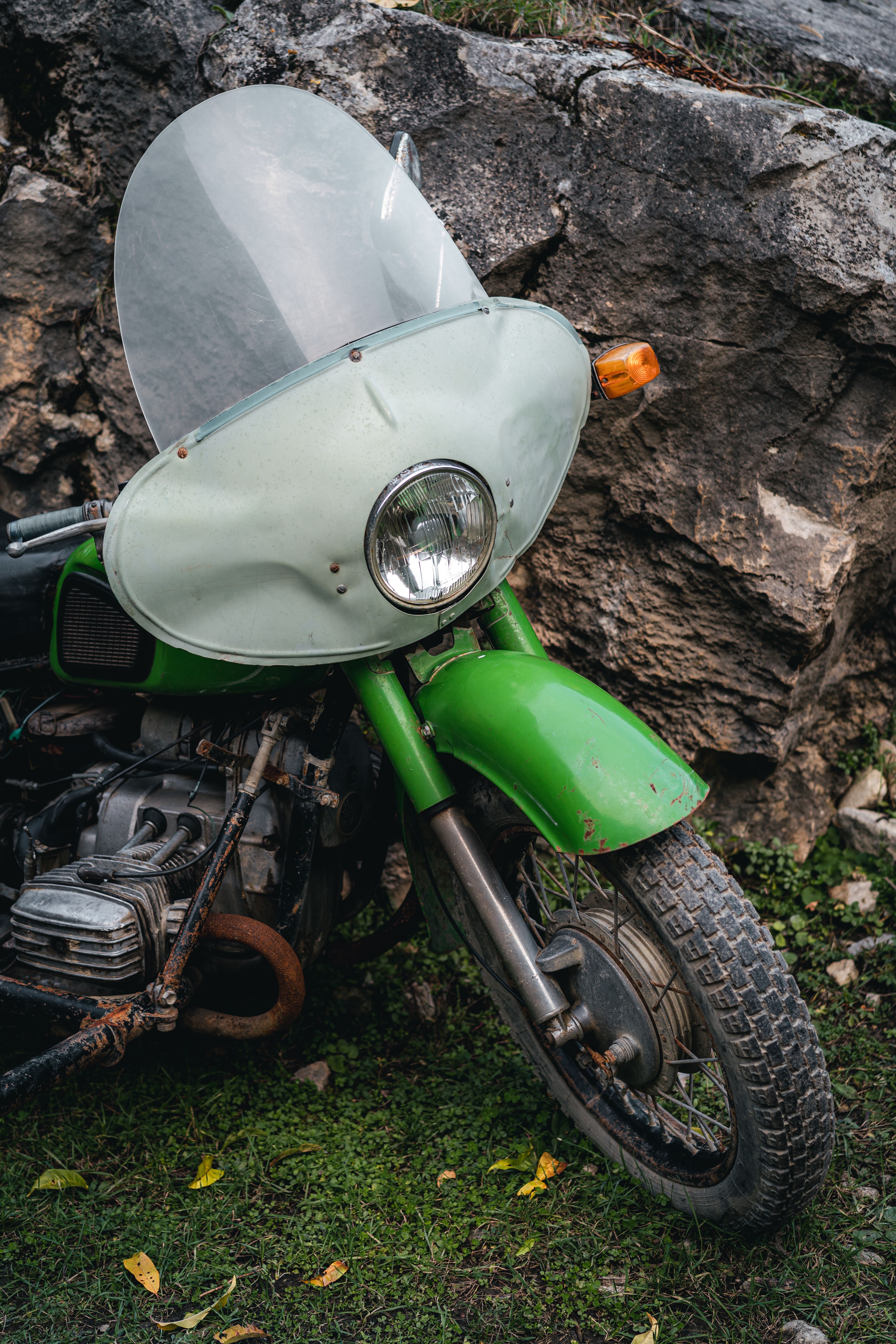 Close-up of a classic green motorcycle with windshield parked near rocky ground.