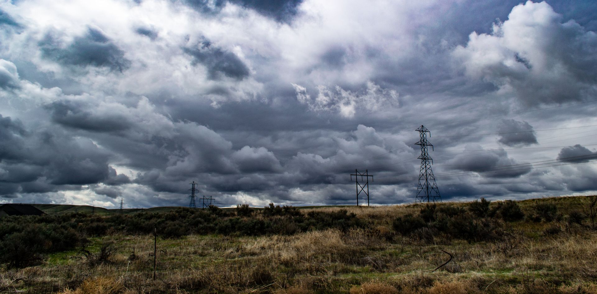 Stormy clouds hover above a grassy field with power lines, showcasing energy and nature.
