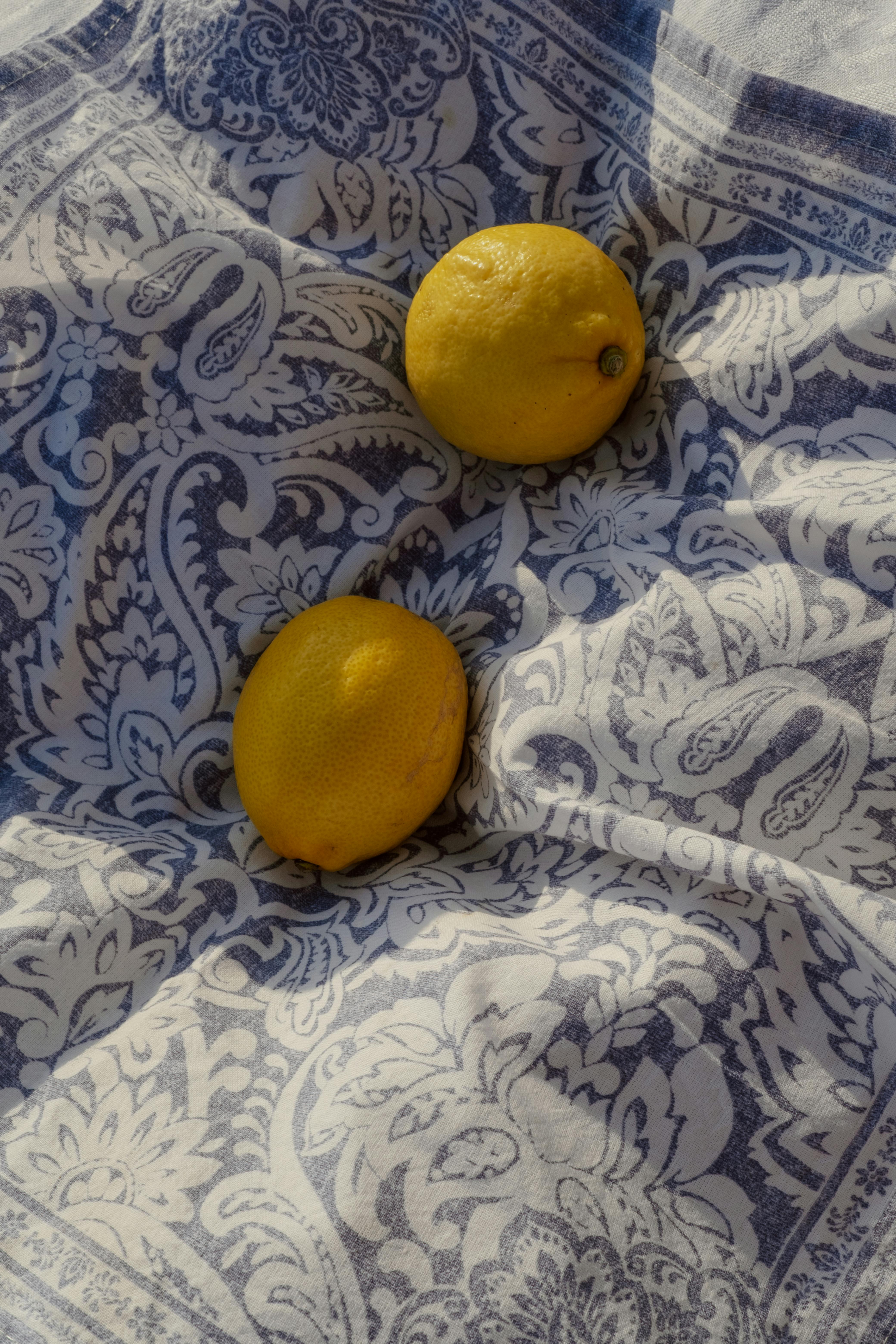 Two fresh lemons displayed on a patterned paisley cloth, capturing a rustic aesthetic.