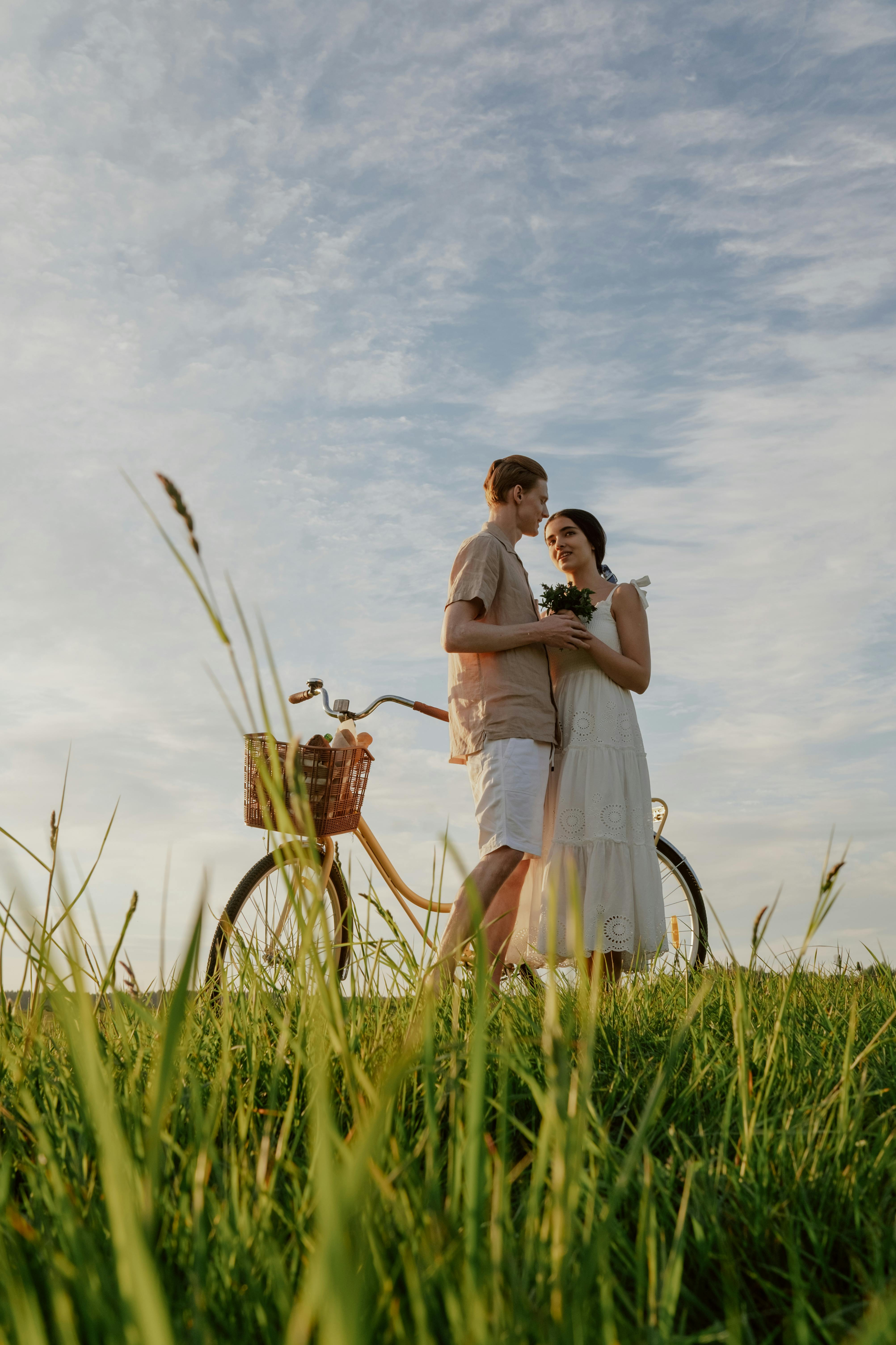 A couple sharing a romantic moment in a sunny field with a bicycle.