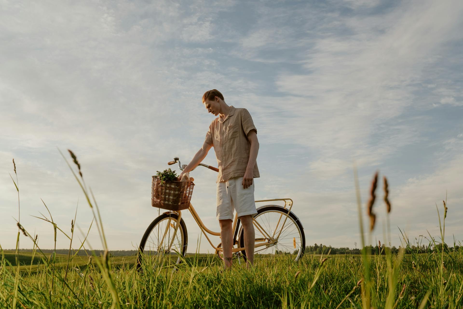A man stands with a bicycle in a sunny meadow, enjoying a serene summer day.
