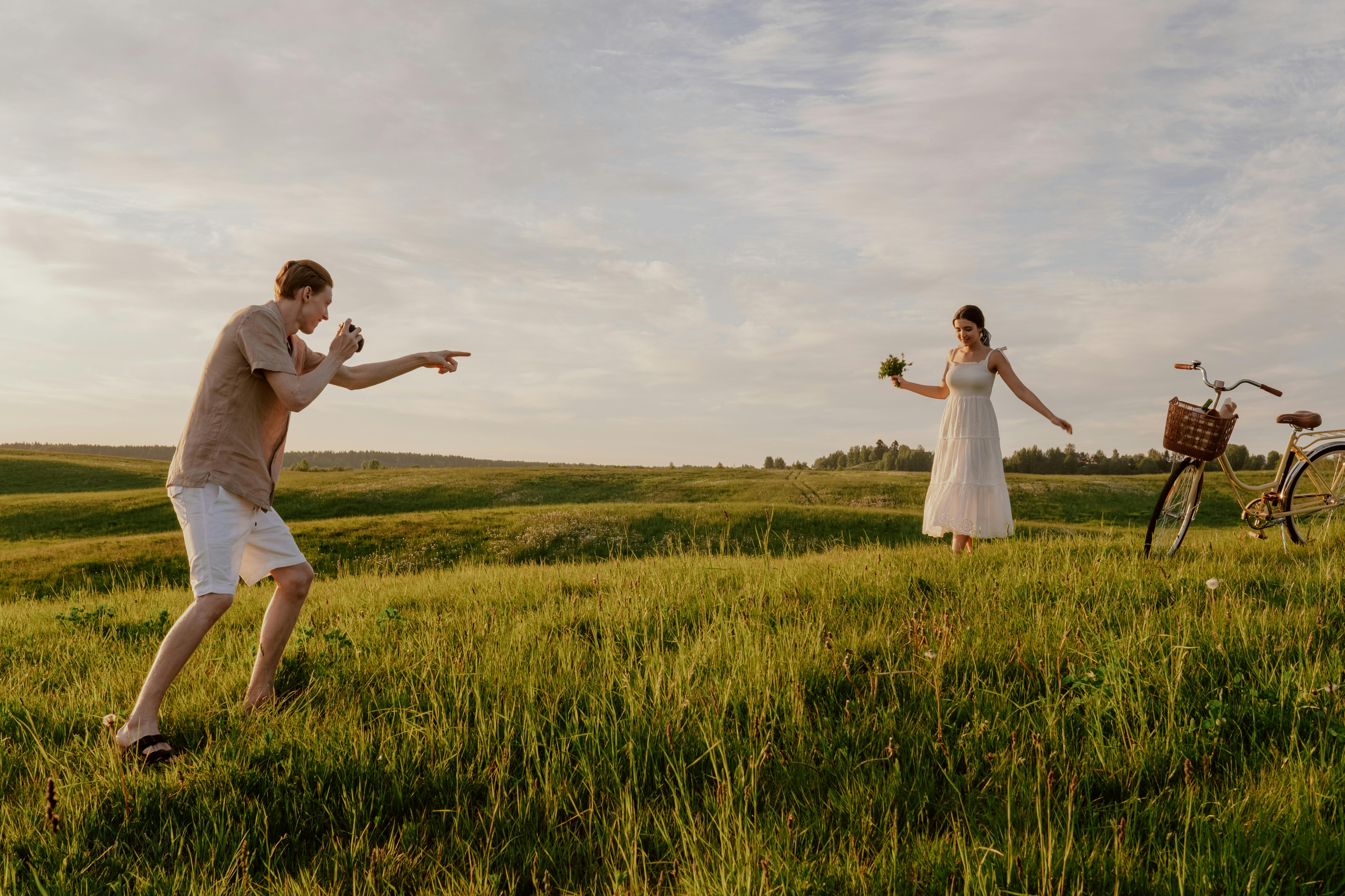 A couple takes photos in a sunny meadow, embracing nature and joy on a summer day.