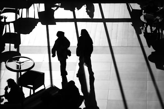 Black and white silhouette of people walking in an airport terminal with strong shadows.