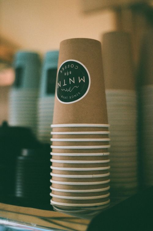 Free A stack of branded paper coffee cups in a cozy café setting with a blurred background. Stock Photo