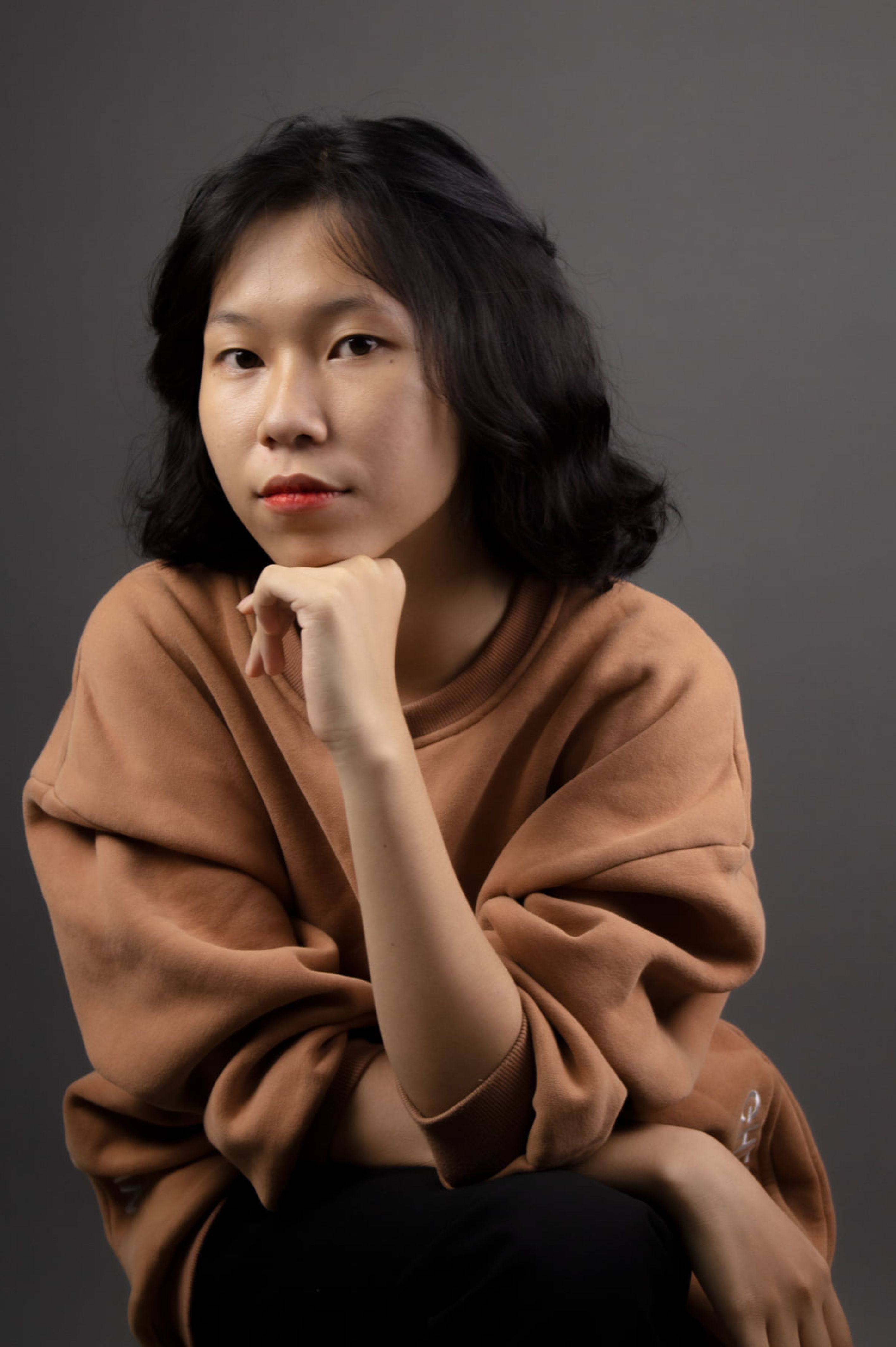 Studio portrait of a thoughtful young woman with hand on chin, gazing forward.