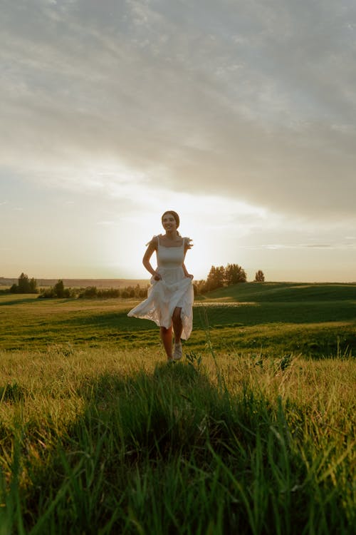 Woman in White Dress Running Through Meadow at Sunset