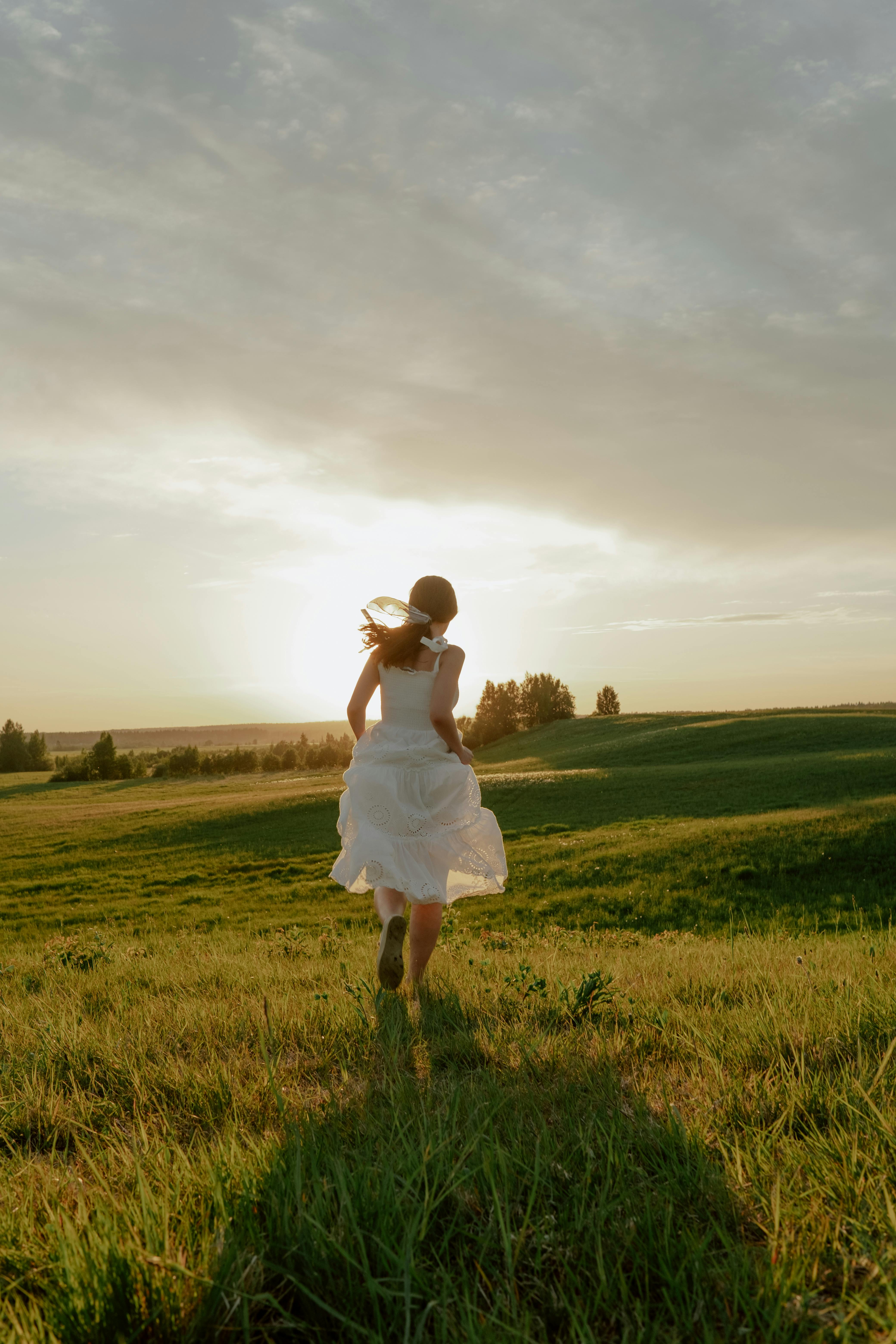 woman in white dress running through meadow at sunset