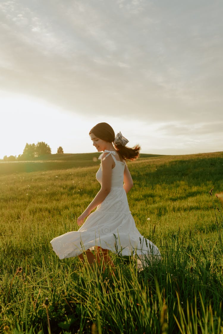 Woman In White Dress Spinning In Meadow At Sunset