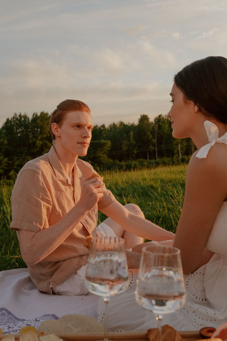 An engaged couple sharing a picnic at sunset in a meadow